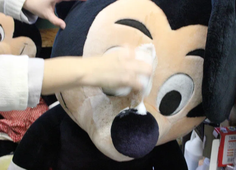 キャラクターのぬいぐるみの顔を手作業で丁寧に洗浄する様子