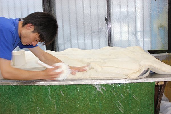 布団を作業台に広げ、泡で洗浄する工程。